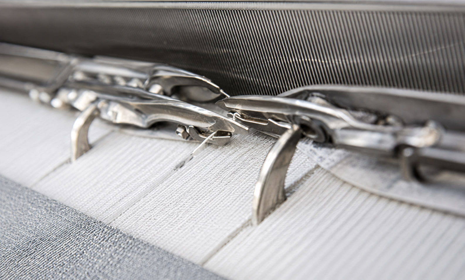 Weft grippers passing through the reed on a Dornier rapier loom, woven filtration fabric forming below
