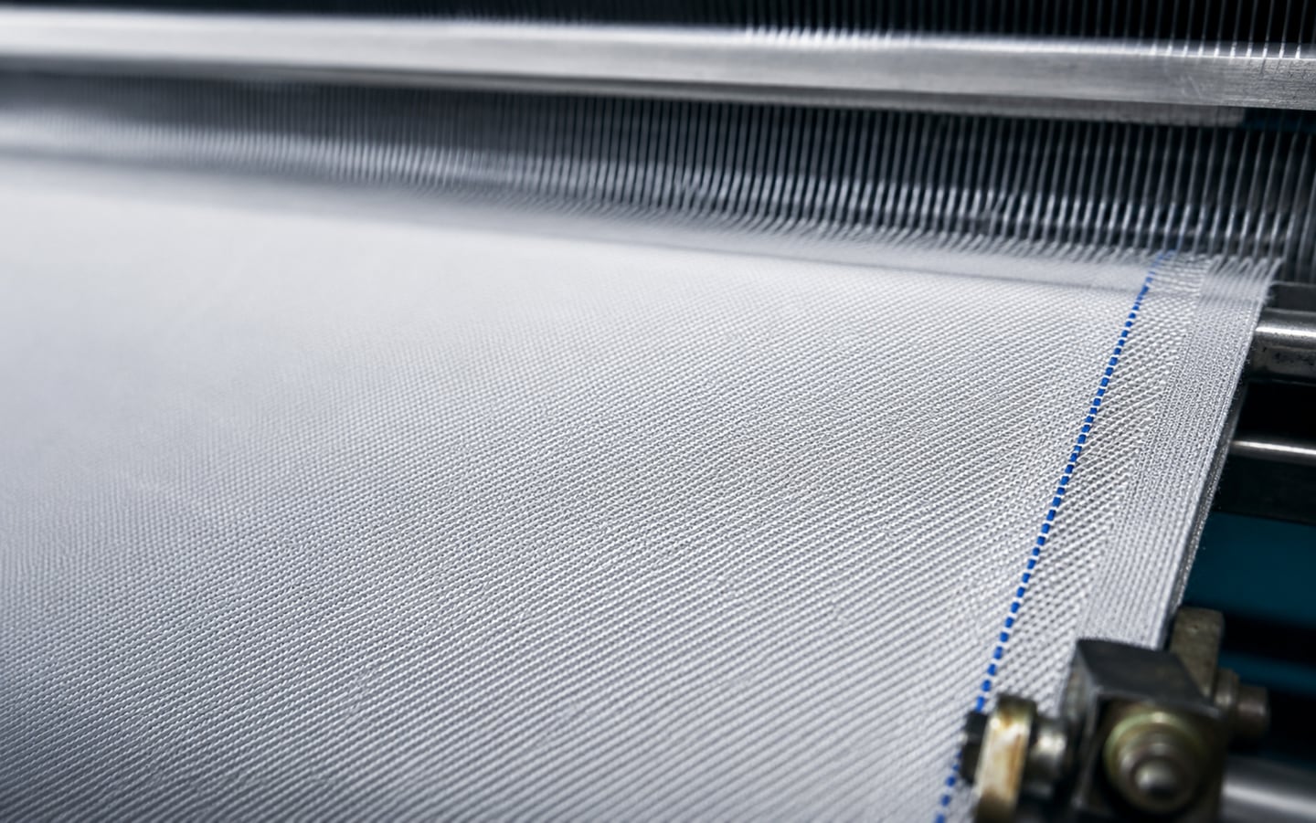Woven filtration fabric running off the loom, the reed above it and a blue selvedge marker thread along the edge