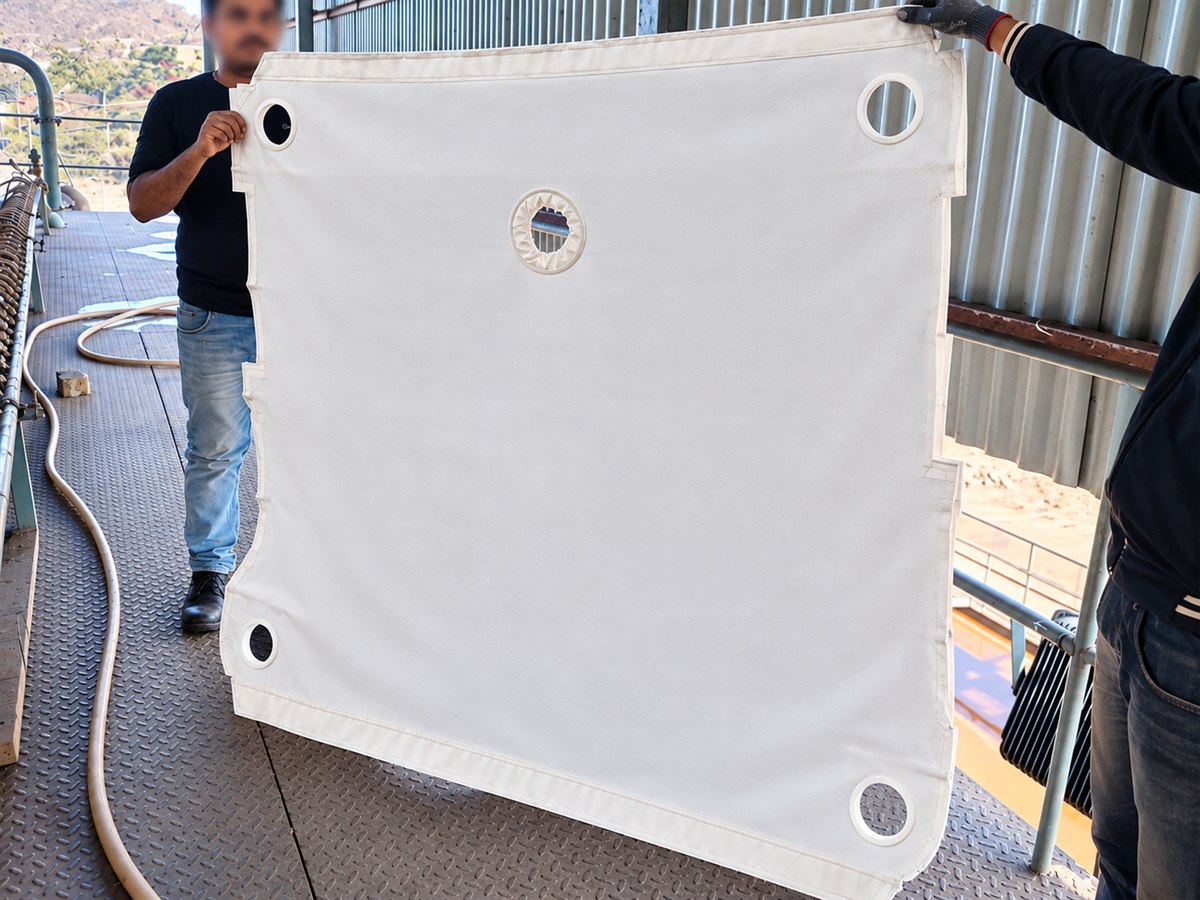Two people holding a full-size DFR filter press cloth open between them, feed neck and corner eyelets visible